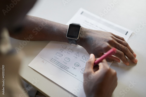 High angle closeup of unrecognizable African-American boy writing in notebook while taking math test in school, focus on smartwatch, copy space