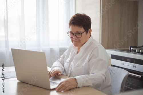 Serious confident middle aged female journalist sitting at desk with laptop, making research. Attractive mature woman working from home.