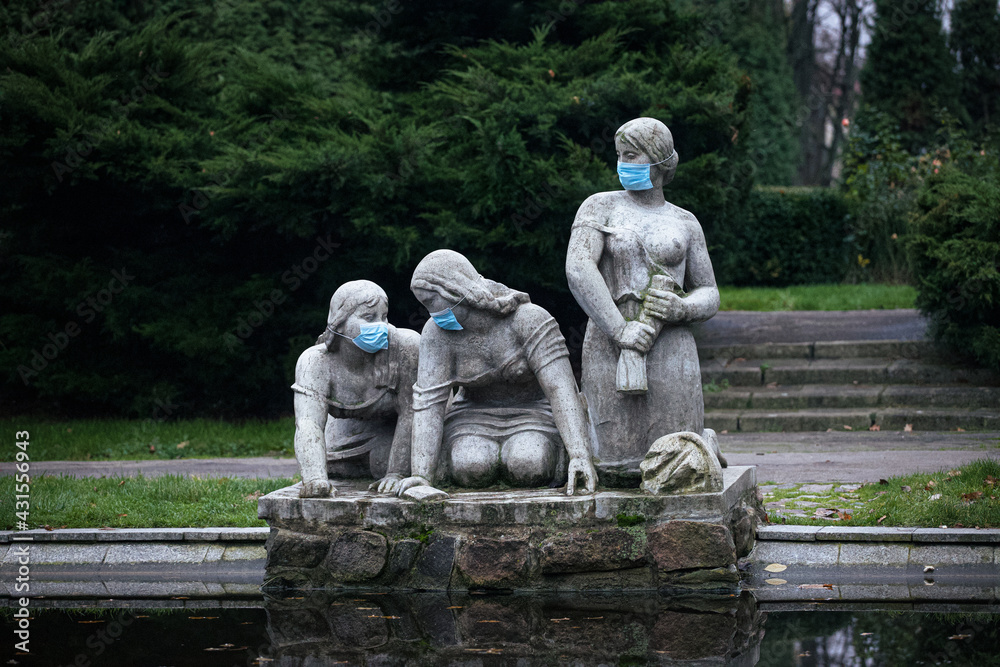 Figures of a women standing in a public park with protective masks on.