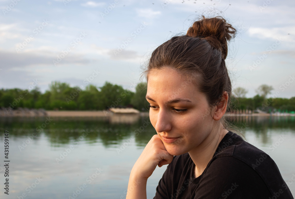 Portrait of a beautiful  natural young woman with a haïr bun and a downcast look, contemplating, river water background