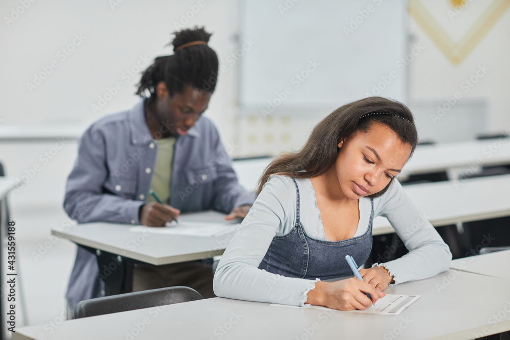 Students taking test in school class with focus on young African-American woman sitting at desk in front, copy space Students taking test in school class with focus on young African-American woman sitting at desk in front, copy space