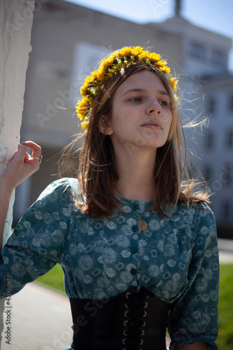 The girl in a blue dress and glasses wove a wreath of yellow dandelions