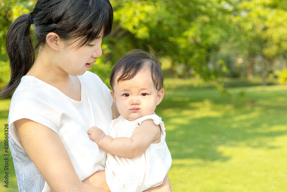 新緑の樹木を背景に赤ちゃんを抱くお母さん。幸せ,愛情,育児イメージ 新緑の樹木を背景に赤ちゃんを抱くお母さん。幸せ,愛情,育児イメージ