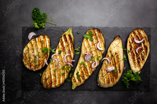 Grilled eggplant slices, garnished with fresh herbs, on black background, top view