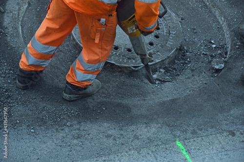 Straßenarbeiter mit orangefarbener Hose arbeitet mit Presslufthammer an einem Kanaldeckel