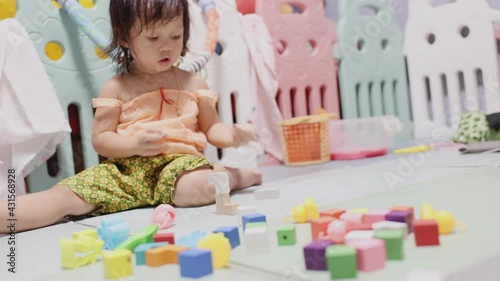 A small child, an Asian woman, was having fun playing plastic toys and wooden blocks in her home.