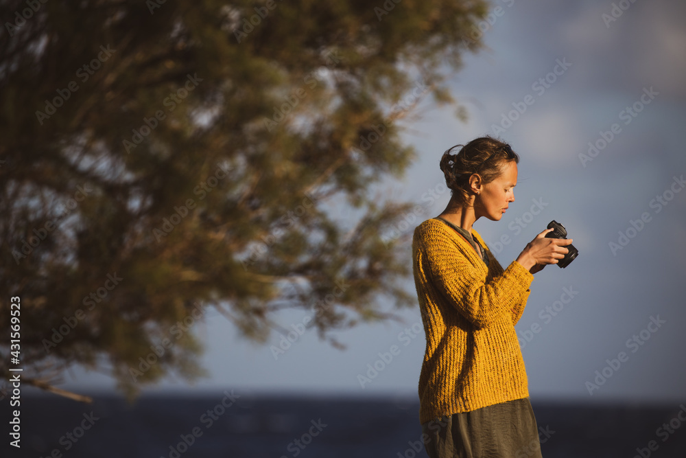 Pretty, young woman with a mirrorless camera, taking photos by the sea