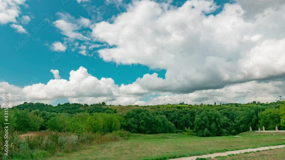 Summer landscape of park with green trees and blue clouded sky filmed in timelapse. There is path and lawn where people are walking. White fluffy cumulus is flying. Theme of spending weekend outdoors. Summer landscape of park with green trees and blue clouded sky filmed in timelapse. There is path and lawn where people are walking. White fluffy cumulus is flying. Theme of spending weekend outdoors.