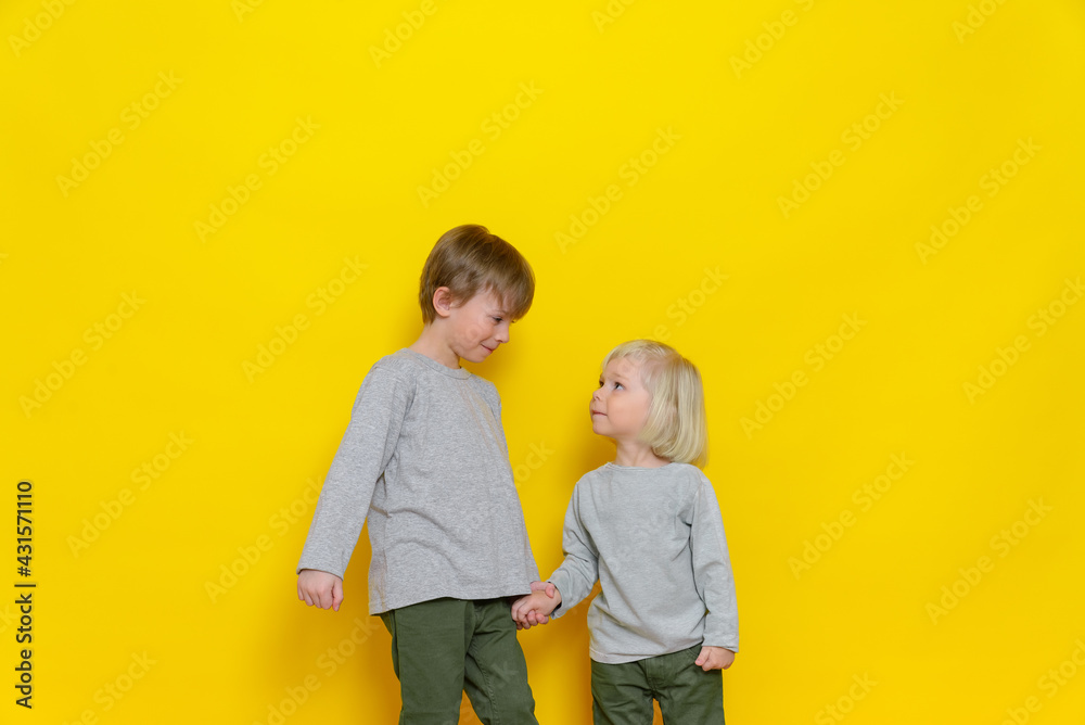Two little cute boys hold hands and look at each other with a smile. Cheerful and mischievous children. Colored background. Two little cute boys hold hands and look at each other with a smile. Cheerful and mischievous children. Colored background.