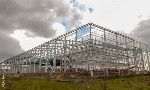 Metal framework of a partially fabricated large warehouse under construction. Landscape image with space for text. Overcast, clouded skyline. Oxfordshire, England. © Steve