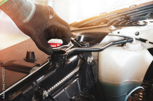 Mechanic hand is opening the radiator cap to check the coolant level of the car radiator photo