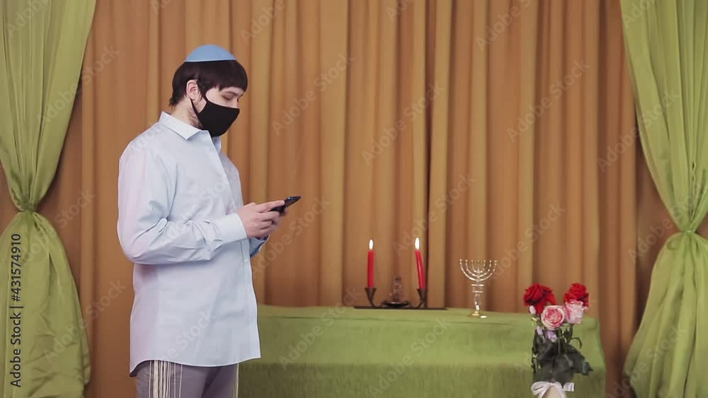 Before the chuppah ceremony, a Jewish groom in a protective mask in a synagogue hall dials an SMS by phone Before the chuppah ceremony, a Jewish groom in a protective mask in a synagogue hall dials an SMS by phone