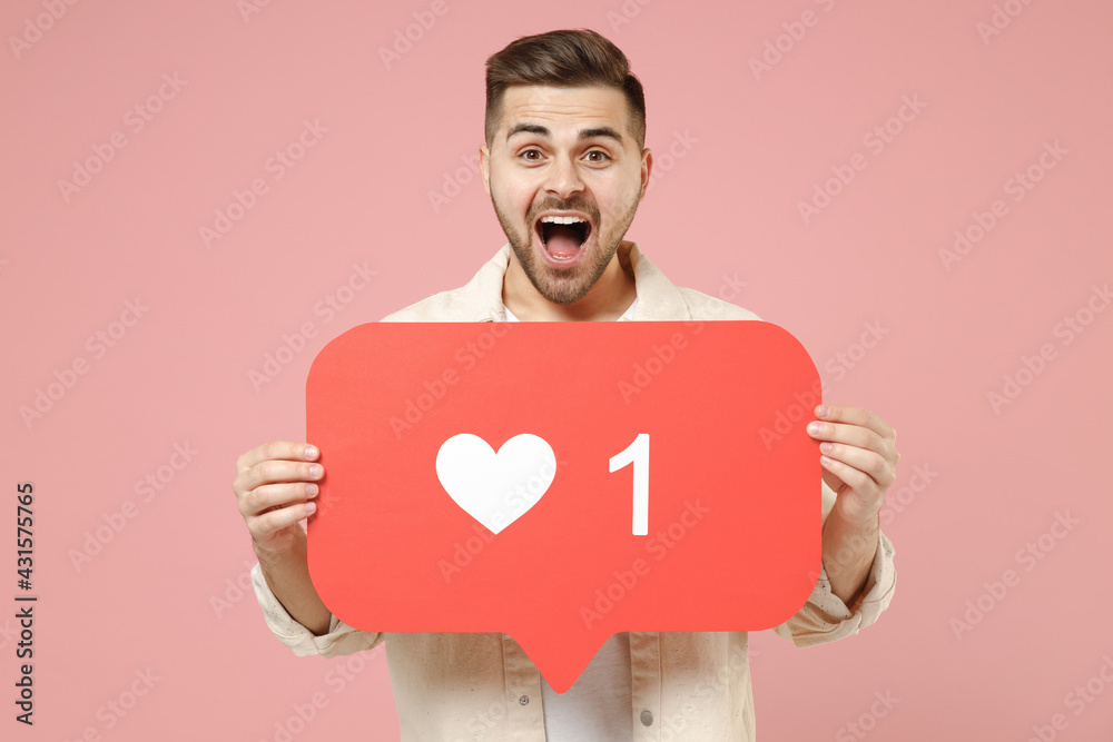 Φωτογραφία Young fun excited caucasian man 20s wearing jacket white t-shirt huge like sign from social network heart form blink isolated on pastel pink color background studio portrait