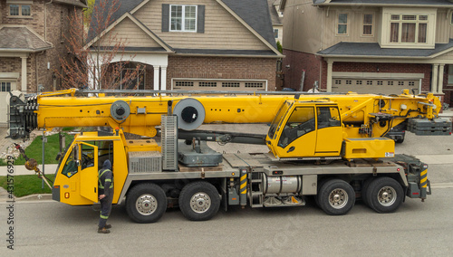 A large truck crane is getting ready for work in a residential area next to the house