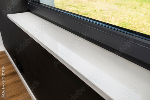 Newly installed white conglomerate window sill inside the room, on the black wall.