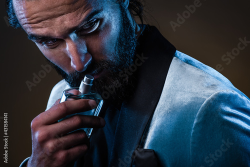 Beautiful masculine bearded young man holding a bottle of fragrance. Masculine perfume, bearded man in a suit.