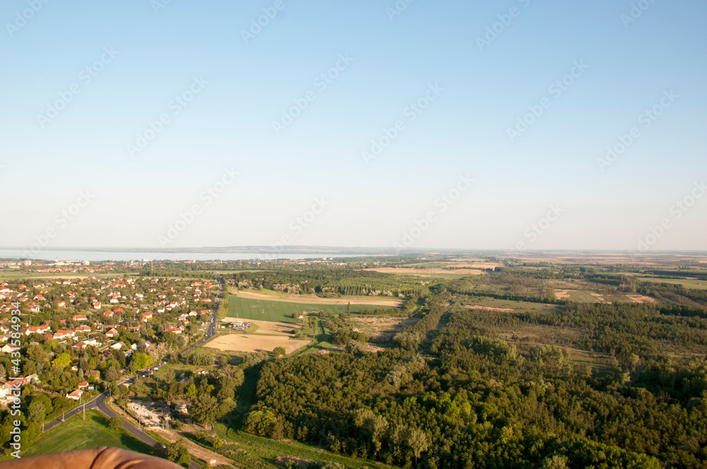Panoramic view from a hot air balloon to town houses, forest and lake on the horizon.