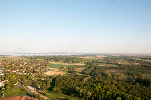 Panoramic view from a hot air balloon to town houses, forest and lake on the horizon.