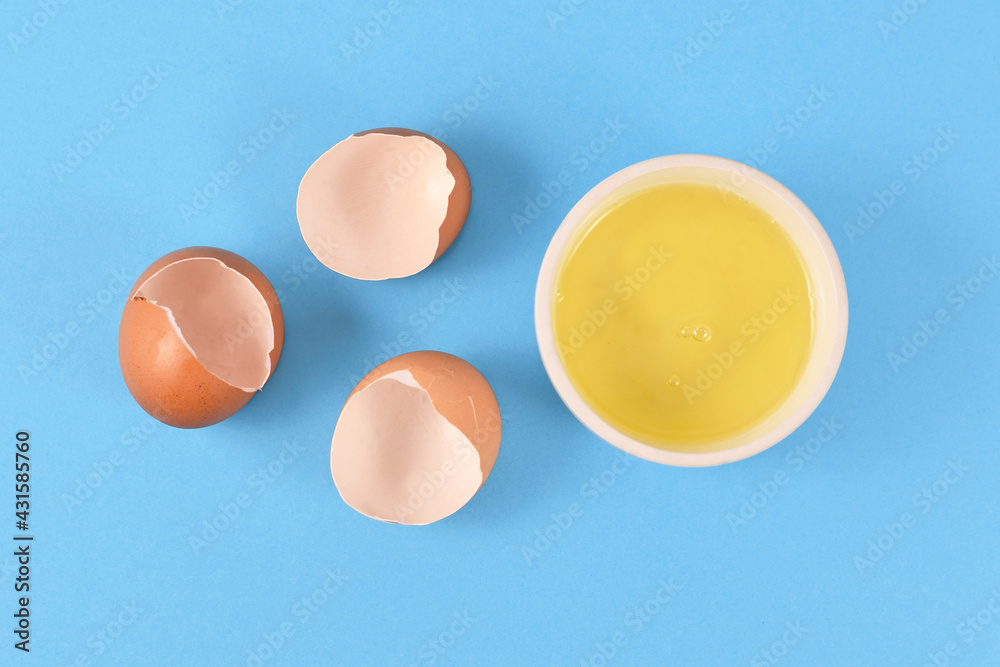 Egg white in bowl next to broken eggshells on yellow background Stock