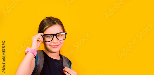 Banner girl kid 7 y.o. glasses with smartwatch looking at camera in isolation on a yellow background. Back to school.