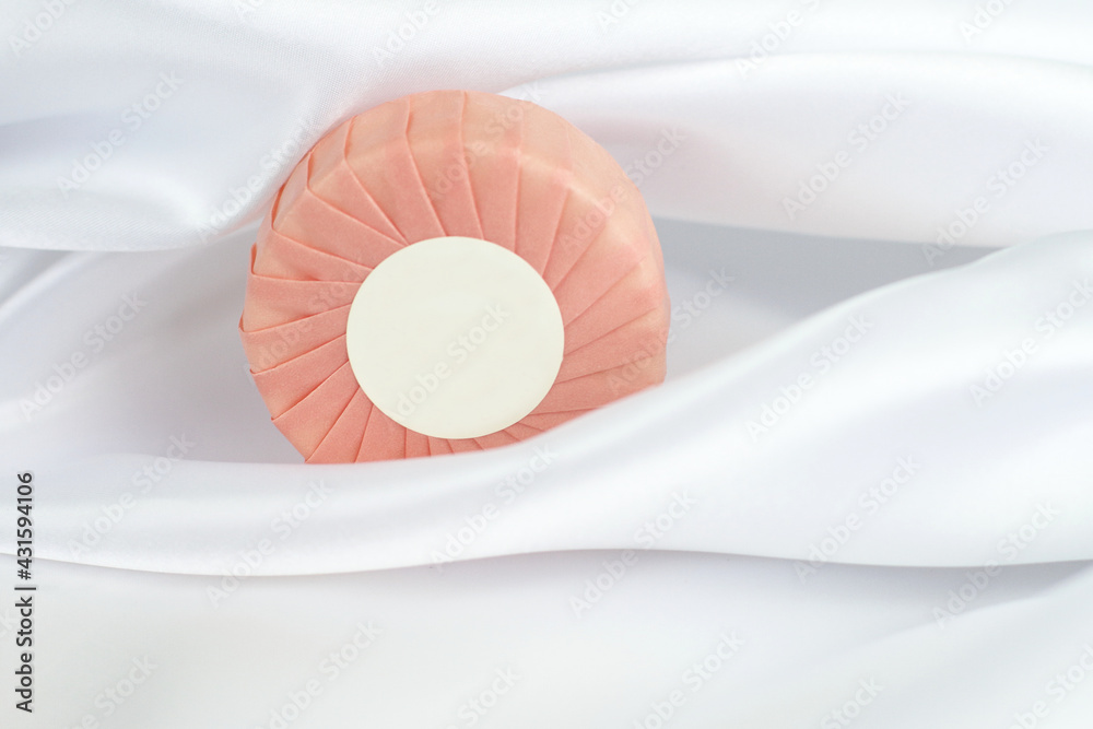 Round solid soap bar in pink paper package on white silk background Round solid soap bar in pink paper package on white silk background