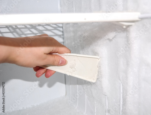 Woman cleanes the refrigerator. Woman's hand with ice scraper. Defrosting of freezer.