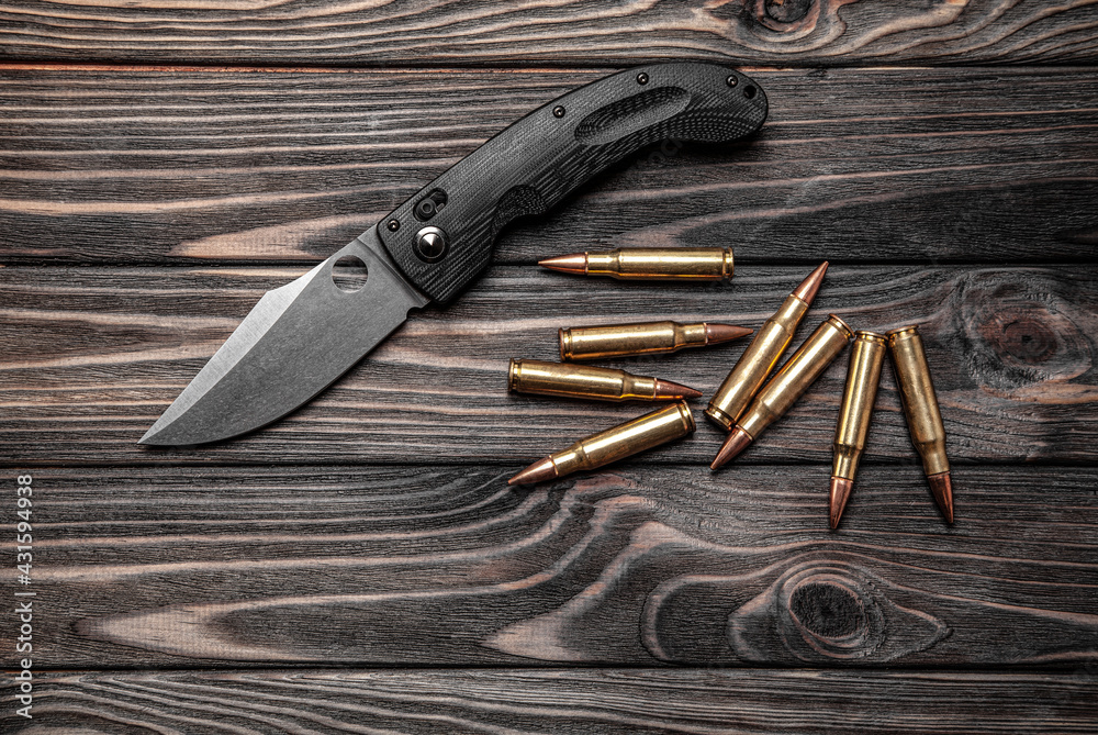 Pocket folding knife and a few rifle cartridges on a wooden back Pocket folding knife and a few rifle cartridges on a wooden back