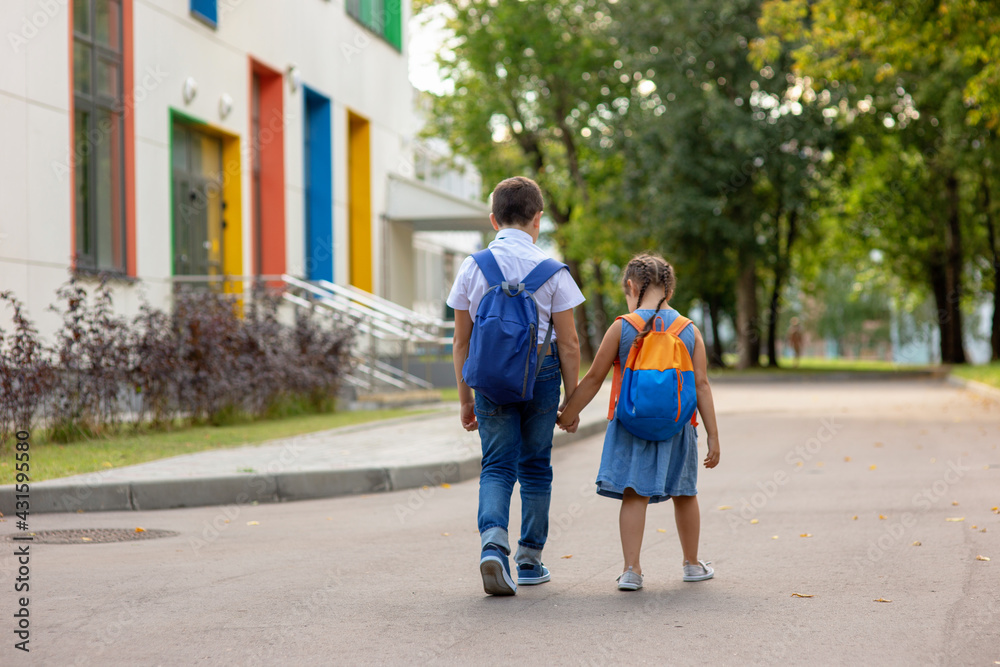 two schoolchildren, a little girl and a boy in a with backpacks go on the way to school.
