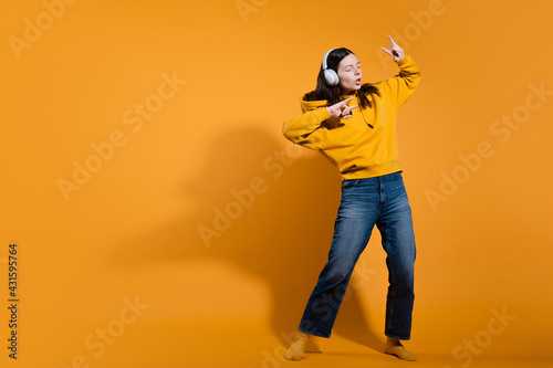 Happy dancing music lover. A young woman in a yellow hoodie with white wireless headphones,
