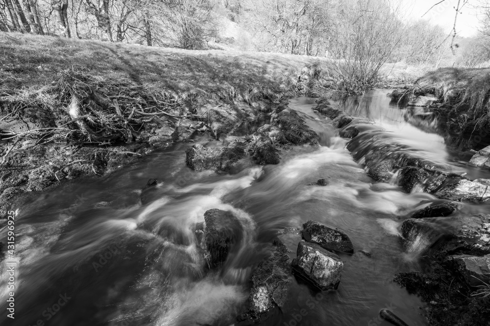Obraz premium Long exposure of the Weir Water river flowing through the valley at Robbers Bridge in Exmoor National Park
