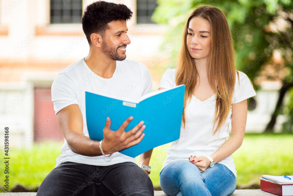 Two students studying together sitting on a bench outdoor Two students studying together sitting on a bench outdoor
