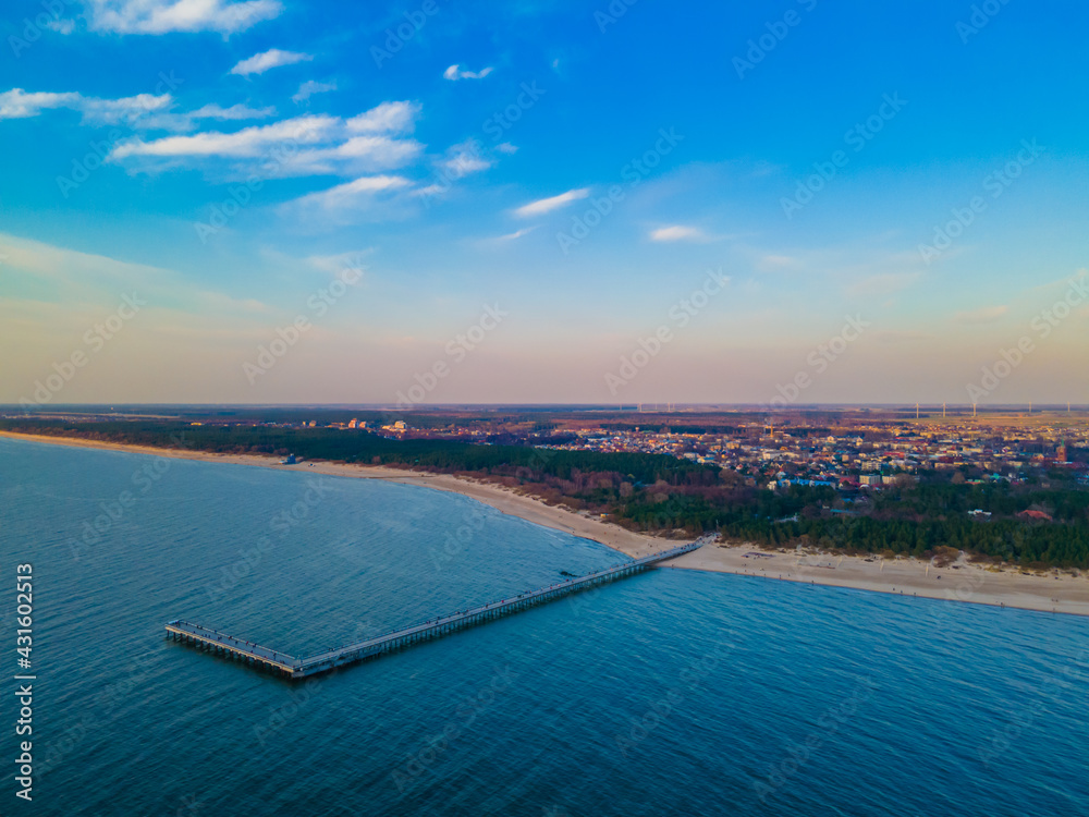 Aerial view of Palanga pedestrians bridge to the wavy sea and coastline with sandy beach and blue cloudy sky during a sunset. View from the sea side