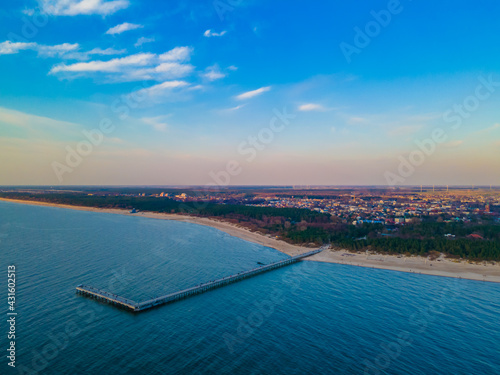 Aerial view of Palanga pedestrians bridge to the wavy sea and coastline with sandy beach and blue cloudy sky during a sunset. View from the sea side © Audrius