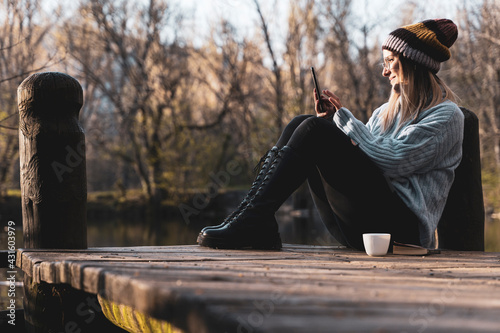 women relaxing in the wooden pier lake with smartphone.