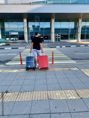 Moscow, Russia - August, 2020: Male is carrying red and blue luggage in street before trip