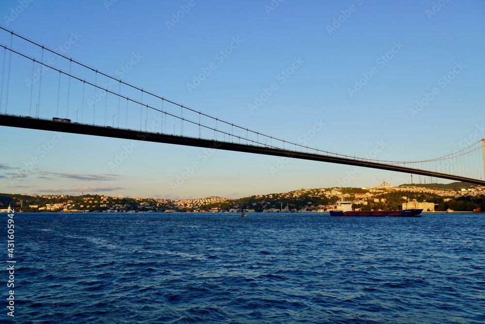 Fototapeta premium Tourist boats sail under the bridge in Istanbul. Traveling on the Bosphorus. Panoramic view, View of the First Bosphorus Bridge sailling Bosporus.