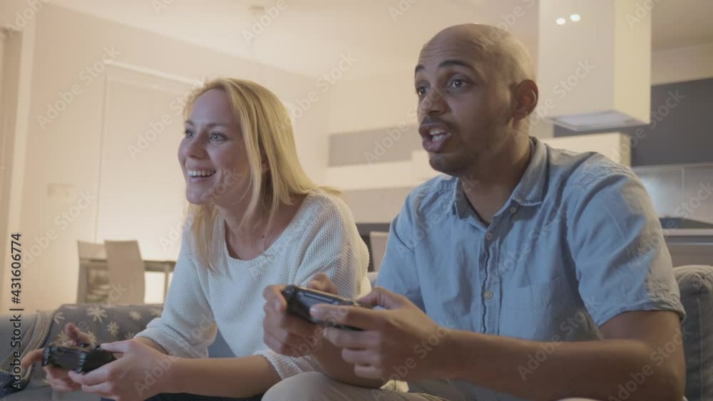 Middle shot of a smiling couple, Caucasian girl and African-American man talking and playing video games using gamepads Middle shot of a smiling couple, Caucasian girl and African-American man talking and playing video games using gamepads