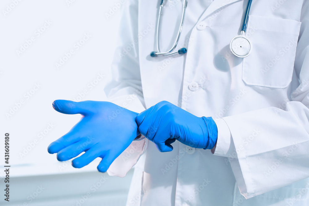 Doctor with stethoscope in a medical gown puts on protective gloves in a hospital Doctor with stethoscope in a medical gown puts on protective gloves in a hospital