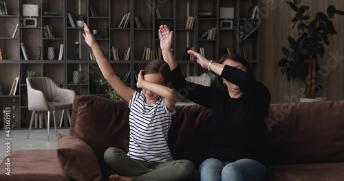 Grandmother and little granddaughter having fun performing dab gesture, making movements seated on sofa in living room. Multi generational family celebrating victory engaged in funny activity at home photo