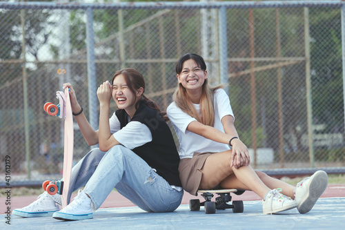 Happy Two Asian Girls Teenage Friends With Skateboard In Sunshine. Playing Together On Summer Day and Skateboarding Lifestyle.