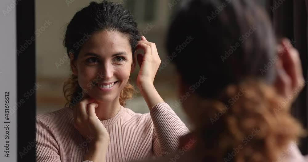 Groomed woman standing in front of mirror fix hair, touch perfect flawless fresh smooth face skin feel satisfied after anti-ageing skincare cosmetic procedure. Morning routine, self-admiration concept
