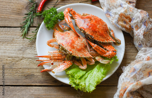 Fresh seafood crab on white plate cooking food in the restaurant, Steamed or boiled Blue Swimming Crab ocean gourmet with chili herb and spices lemon and rosemary on wooden dining table, top view