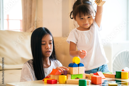Asian girl and her mixed race sister playing wooden color block an education toy at living room. a family activity concept