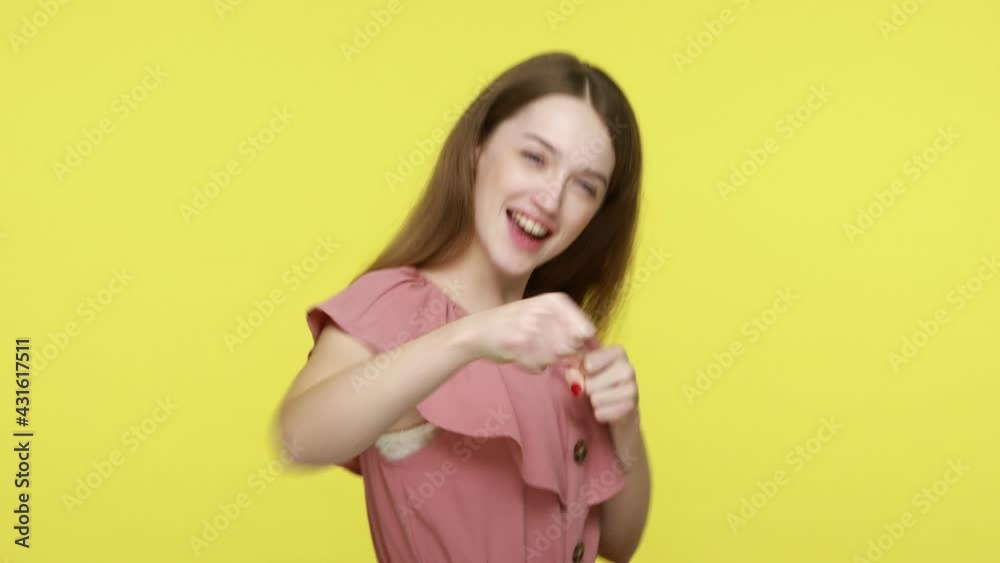 Brave beautiful brown haired female in elegant dress punching fists to camera, boxing with positive facial face expression, self defense concept. Indoor studio shot isolated on yellow background. Brave beautiful brown haired female in elegant dress punching fists to camera, boxing with positive facial face expression, self defense concept. Indoor studio shot isolated on yellow background.