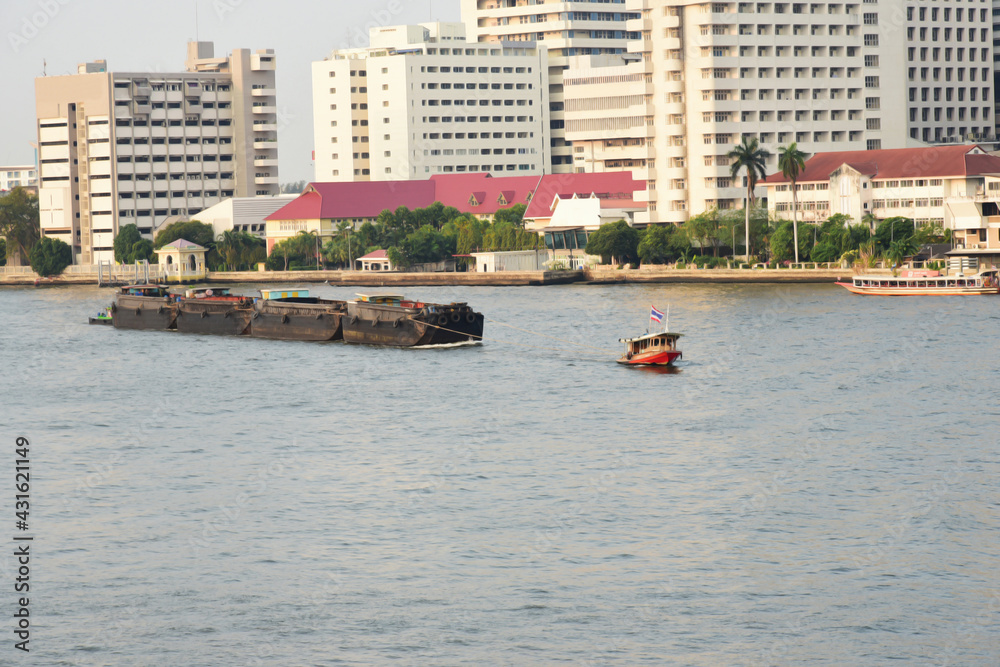 Obraz premium Sand boat pulled by a tugboat is shipping in the Chao-pha-ya river form Ayu-tha-ya province to Bangkok is a long time local transport business in Thailand.