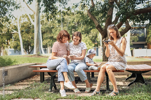 Three women friends with baby strollers reading text message in park