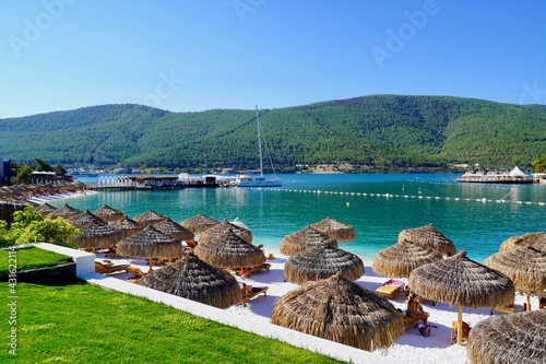 Fototapeta Naklejka Na Ścianę i Meble -  Bodrum, Turkey - August, 2020 Snow-white beach of Lux Hotel with emerald water of Aegean Sea. Yachts. People sunbathing on the beach. Sunbeds on the beach. Relaxing Deluxe Leisure Conception. Paradise