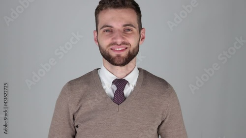  Young manager smiling, looking at camera with isolated grey background, he wears a brown sweatshirt