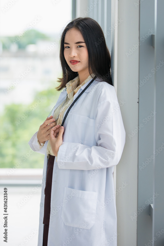 Vertical full-body portrait shot of attractive smiling professional young adult Asian doctors wearing a laboratory white coat standing and looking at the camera with a stethoscope around the neck Vertical full-body portrait shot of attractive smiling professional young adult Asian doctors wearing a laboratory white coat standing and looking at the camera with a stethoscope around the neck
