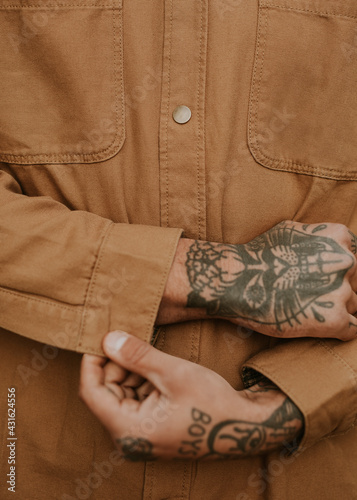 Tattooed man buttoning his brown shirt closeup